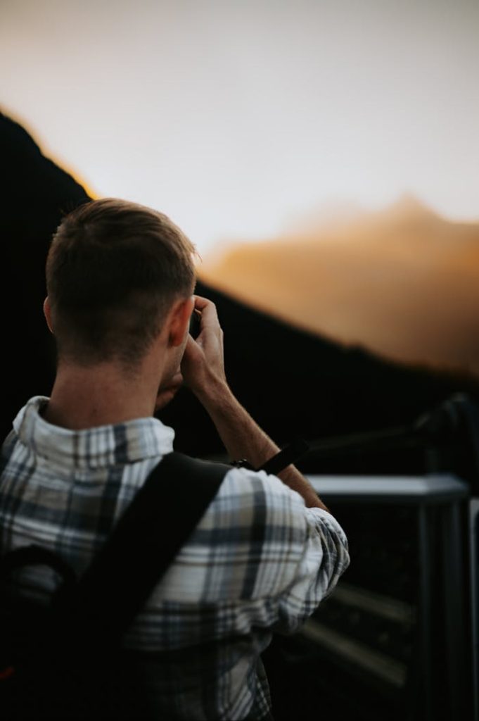 Back view of a male photographer capturing a sunset scene outdoors.